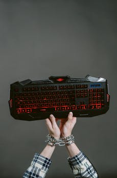 A dramatic concept image of chained hands holding a glowing gaming keyboard, symbolizing technology dependency.