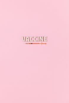 Creative vaccine text and syringe on pastel pink background.