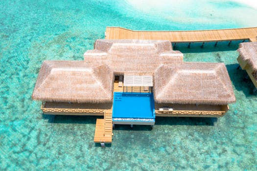 Aerial view of a thatched luxury water villa with pool in the clear Maldives waters.