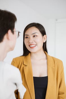 Confident young woman in a mustard blazer smiling warmly in an office environment.