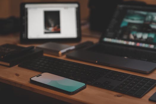 A contemporary workspace setup featuring a laptop, smartphone, and tablet on a wooden desk.