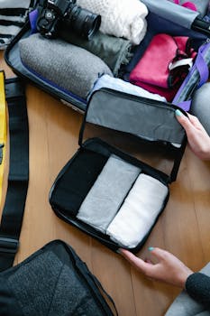 A person efficiently packs clothing and essentials into a suitcase for travel, showcasing organization and preparation style.