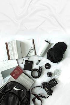 Flat lay of travel essentials featuring a camera, passport, and notebook on white background.