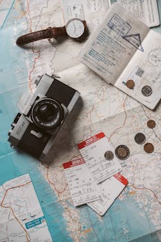 Flat lay travel essentials including passports, tickets, and a vintage camera on a world map.
