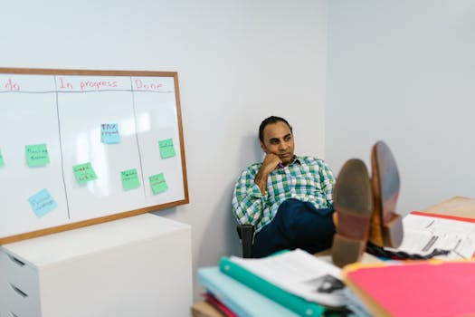Man in casual attire relaxing at his office desk, contemplating work on a kanban board.