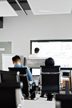 Professionals collaborating in an office with whiteboard brainstorming and coding on computers.