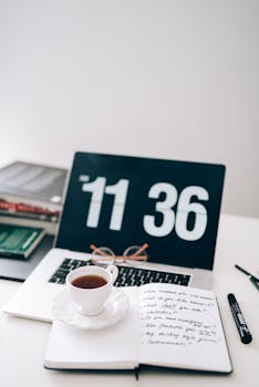 Stylish workspace featuring a coffee cup, notebook, and digital clock on a laptop.
