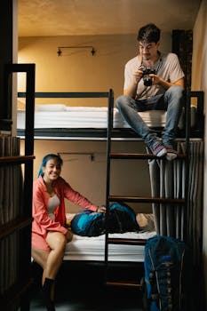 Two young travelers enjoying their hostel stay with bunk beds and backpacks.